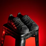 Championes Adidas modelo Superstar, color negro con las icónicas tres tiras laterales en acabado iridiscente y puntera de goma clásica.