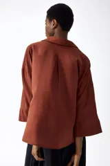 Camisa de mezcla de lino y viscosa color terracota, con cuello abierto, escote en V con botonadura frontal, hombros caídos y mangas tres cuartos holgadas.