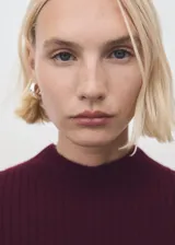 Vestido midi de punto acanalado en color bordó, con cuello perkins y mangas largas acampanadas. Presenta un diseño entallado al cuerpo.