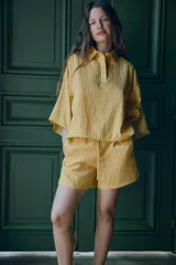 Camisa de corte holgado confeccionada en mezcla de lyocell, con estampado de rayas verticales en tonos amarillos y blancos. Presenta cuello solapa, cierre frontal parcial con botones y mangas anchas por debajo del codo.