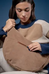 Bolso tipo bandolera de gamuza color marrón, con correa ancha ajustable decorada con tachas metálicas y cierre superior.