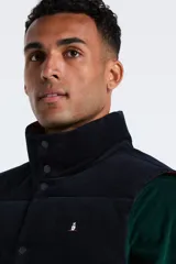 Chaleco reversible de pana, con cierre frontal de botones a presión y cuello alto. Presenta un diseño acolchado con logo bordado en el pecho.