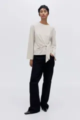 Top de manga larga confeccionado en punto suave, con diseño de hombros caídos, escote redondo y detalle de tira lateral para anudar en la cintura.