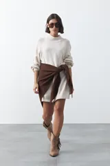Vestido corto de punto en color beige, con cuello alto acanalado, mangas largas con puños ajustados y diseño holgado.