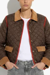 Campera capitoneada color marrón con detalles en pana color tostado en cuello, puños y solapas de bolsillos. Presenta ribetes en color rojo, cierre frontal con botones y diseño acolchado.
