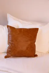 Almohadón decorativo cuadrado, con frente de cuero color marrón y parte trasera de tussor color blanco hueso.