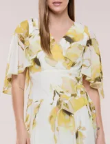Vestido midi de gasa liviana con estampado floral en tonos amarillo y blanco, escote en V cruzado, mangas cortas amplias tipo capa, cintura entallada y falda con vuelo y ruedo irregular.