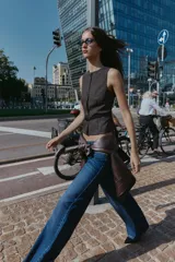 Chaleco jaspeado en tonos grises, con cuello redondo y sin mangas. Presenta cierre frontal con botones dorados y un cinturón fino negro con hebilla dorada.