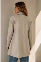 Trench de cuero ovino color cemento, de diseño clásico con solapa en el pecho, bolsillos laterales ojal y cierre frontal con botones.