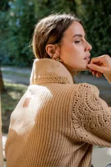 Sweater de punto color gris claro, con cuello amplio tipo solapa y detalles de tejido crochet en los hombros y mangas. Presenta mangas largas con puños ajustados y diseño de corte holgado.