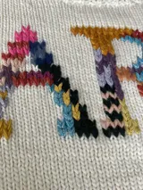 Sweater tejido de lana merino color crudo con bordado multicolor con la palabra "FARRA" en el frente.