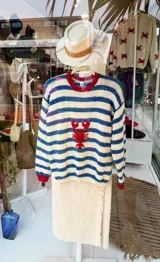 Sweater de lana tejido a mano con diseño a rayas horizontales en color crema y azul, cuello y puños en color rojo, y bordado central de una langosta roja.