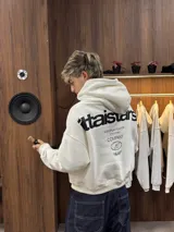 Hoodie de color blanco con capucha, diseño de corte holgado y estampado gráfico en la espalda con tipografía negra.