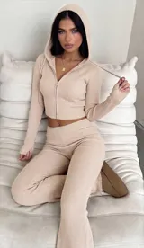 Conjunto de dos piezas compuesto por un buzo tipo hoodie corto con cierre frontal y un pantalón de tiro alto, ambos confeccionados en tejido de punto acanalado color beige.