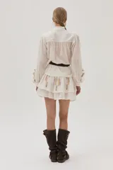 Falda corta de color blanco con diseño de doble volado y delicados bordados en tonos suaves que aportan movimiento y estilo.