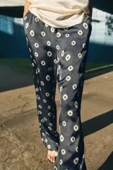 Pantalón de tiro medio con cintura elástica y bolsillos ocultos en costura. Presenta un diseño de corte recto con dobladillo ancho en el bajo y un estampado geométrico sobre fondo oscuro.
