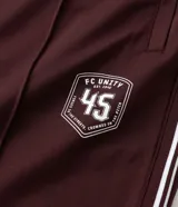 Pantalón deportivo color bordó con rayas blancas laterales, cintura elástica con cordón ajustable, bolsillos laterales y logo pequeño en el muslo.