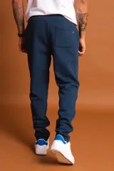 Pantalón de jogging azul piedra con cintura elástica ajustable mediante cordón negro y puños en los tobillos. Presenta un pequeño parche con logo en el lateral.