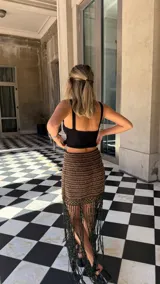 Falda tejida a mano en crochet, con diseño a rayas horizontales en tonos marrón y negro con hilos de lurex dorado. El ruedo presenta una cascada de flecos largos y finos en color negro.