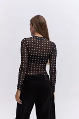 Body de manga larga confeccionado en tejido mesh transparente con estampado de lunares blancos sobre fondo negro. Presenta cuello alto y un diseño ajustado al cuerpo.