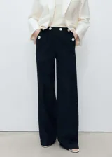 Pantalon de vestir negro de corte recto y tiro medio. Presenta detalle de botones decorativos en contraste en la cintura, bolsillos laterales y bolsillos de ribete en la parte posterior.