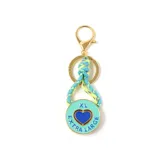 Llavero con dije circular de metal esmaltado en color turquesa, con un corazón azul en el centro y la inscripción 'EXTRA LARGE' grabada. Incluye una cuerda trenzada multicolor y herrajes dorados.