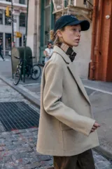 Blazer de corte recto y diseño minimalista, confeccionado en tejido de paño suave color beige. Presenta cuello con solapas clásicas, cierre frontal con un solo botón y dos bolsillos delanteros con solapa.