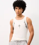 Musculosa de algodón color blanco crudo, de corte ajustado y diseño acanalado. Cuenta con cuello redondo, estampa frontal de cruz y detalles tribales negros en los laterales.