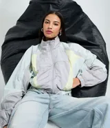 Campera corta viento de mujer de la marca Blue Steel, con cuello alto, mangas largas con puños elásticos y cierre frontal por cremallera. Presenta recortes contrastantes en tonos gris, celeste y amarillo pastel, y ruedo corto con elástico. Confeccionada en poliamida, un tejido sintético ligero y suave.