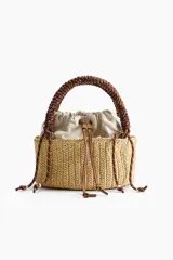 Cartera tipo tote en paja sintética trenzada, con estructura cilíndrica. Cuenta con un bolso interior de lona color beige con cordón ajustable, asa superior trenzada de cuerda marrón y detalles en ecuero.