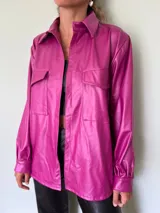 Camisa magenta de cuero sintético, de corte recto, con cuello clásico, cierre frontal con botones a presión, dos bolsillos de parche con solapa en el pecho y mangas largas con puños abotonados.