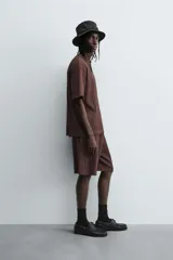 Bermuda de corte relajado color marrón oscuro, confeccionada en tejido jacquard con textura acanalada vertical. Presenta cintura elástica ajustable con cordón, bolsillos delanteros y un bolsillo trasero de plastrón.