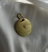 Llavero de bronce color dorado con diseño circular y letra grabada.