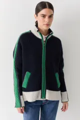 Campera de lana con cierre frontal de doble cursor y cuello alto. Presenta un diseño en bloques de color azul marino, verde y crema, con detalles de tejido trenzado en las mangas y bolsillos laterales con contraste.