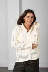 Cárdigan de punto color beige con textura calada de motivos florales, cuello alto, cierre frontal con botones y mangas largas con terminaciones acanaladas.