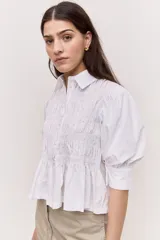 Camisa azul marino de cuello clásico, mangas abullonadas a tres cuartos y detalle fruncido en el frente. Presenta una silueta amplia y diseño corto con vuelo en el ruedo.