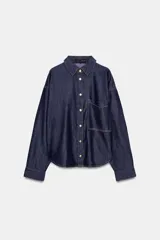 Camisa amplia de denim azul oscuro con cuello solapa, manga larga, bolsillo de plastrón en el pecho y cierre frontal con botones a presión dorados.