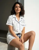 Pijama de algodón compuesto por una camisa de manga corta abotonada con solapas y un short con elástico y lazo en la cintura. Presenta un estampado de lunas y estrellas con detalles de ribetes en contraste.