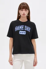 Remera negra de manga corta, con cuello redondo y diseño holgado. En el frente presenta el estampado "GAME DAY" en tonos celestes y azules con tres estrellas.