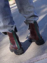 Botas de cuero marrón con suela track de goma negra, cierre lateral en color rojo y detalle de tira trasera al tono.