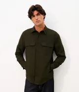 Camisa de manga larga confeccionada en sarga de algodón color verde militar. Presenta cuello inglés, cierre frontal con botones y dos bolsillos con solapa en el pecho.