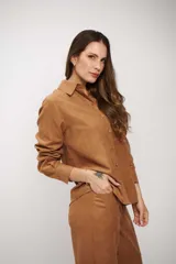 Camisa de manga larga color tostado, con cuello clásico y cierre frontal de botones. Presenta un diseño de corte recto y acabado suave.