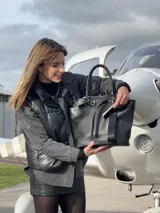 Bolso negro tipo tote de cuero con correa de hombro, hebilla decorativa y etiqueta colgante con la inscripción "NADIA".