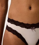 Kit de dos bombachas tipo bikini confeccionadas en microfibra, con detalles de encaje contrastante en los bordes y un pequeño lazo decorativo en el centro. Una pieza es de color beige y la otra de color marrón oscuro.