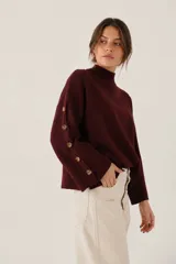 Sweater de tejido de punto color bordó, con cuello alto y detalle de botones decorativos a lo largo de las mangas. Presenta un diseño holgado y mangas largas.