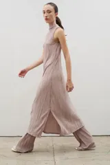 Vestido midi de diseño plisado en color rosado, con cuello alto y sin mangas. Presenta un tajo lateral y corte holgado, diseñado para ser usado en conjunto con pantalones del mismo tejido.