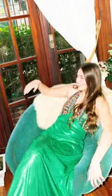 Vestido largo sin mangas con escote en V halter y aberturas laterales (cut-outs) en la cintura. El cuerpo superior presenta un llamativo diseño estampado multicolor, mientras que la falda larga es de tejido texturizado brillante en color verde esmeralda con inserciones godet en el ruedo.