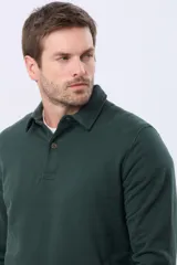 Buzo de felpa color verde oscuro, con cuello tipo polo, cierre frontal parcial con botones y bolsillos laterales. Presenta puños y ruedo acanalados.