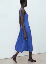 Vestido midi de color azul, con diseño evasé, cuello cuadrado y tirantes anchos. Presenta un corte en la cintura con falda fruncida y cierre de cremallera en la parte posterior.