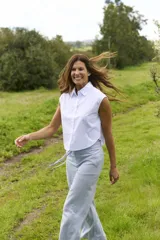 Blusa blanca sin mangas, de corte holgado y diseño corto, con cuello camisero y cierre frontal de botones.